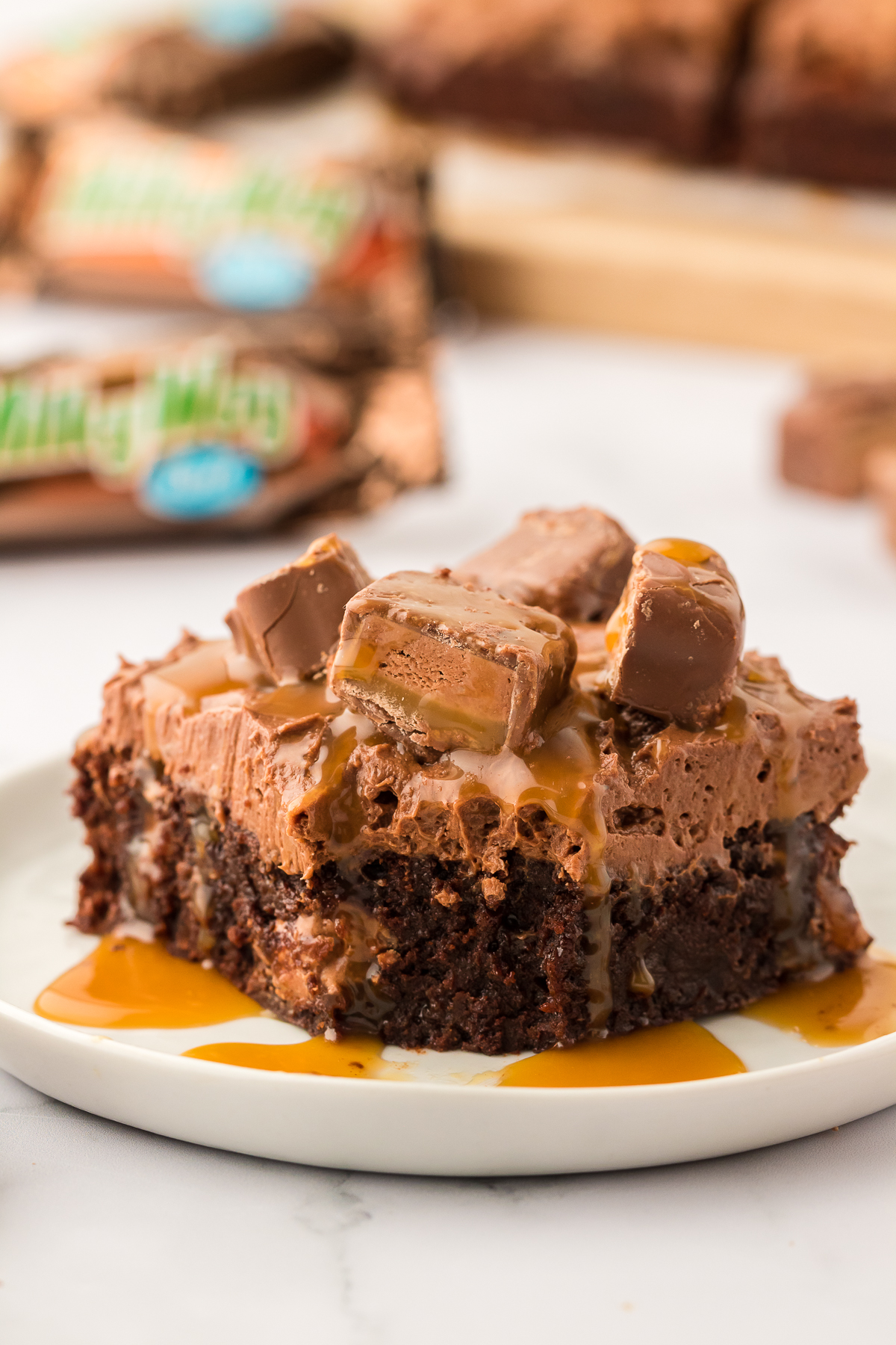 milky way brownie on a plate topped with candy bars and caramel sauce