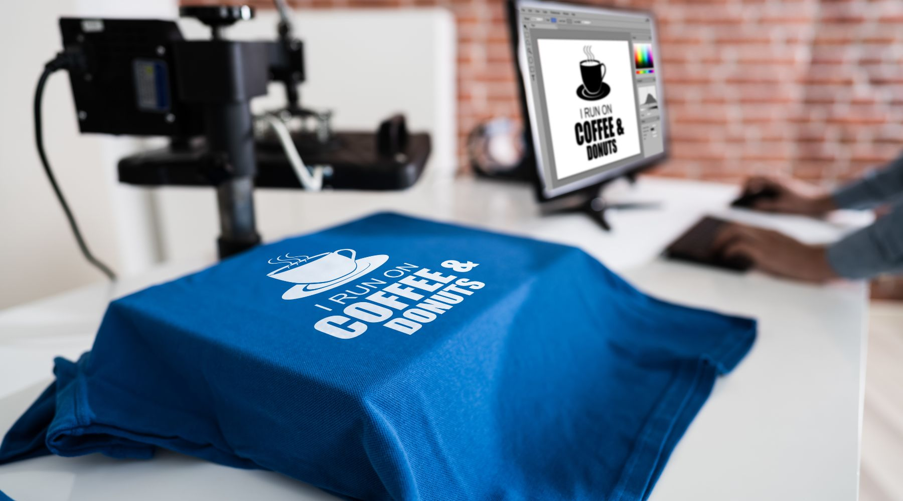 Graphic design process with a blue T-shirt reading 'I run on coffee and donuts' next to a matching screen design on a computer.