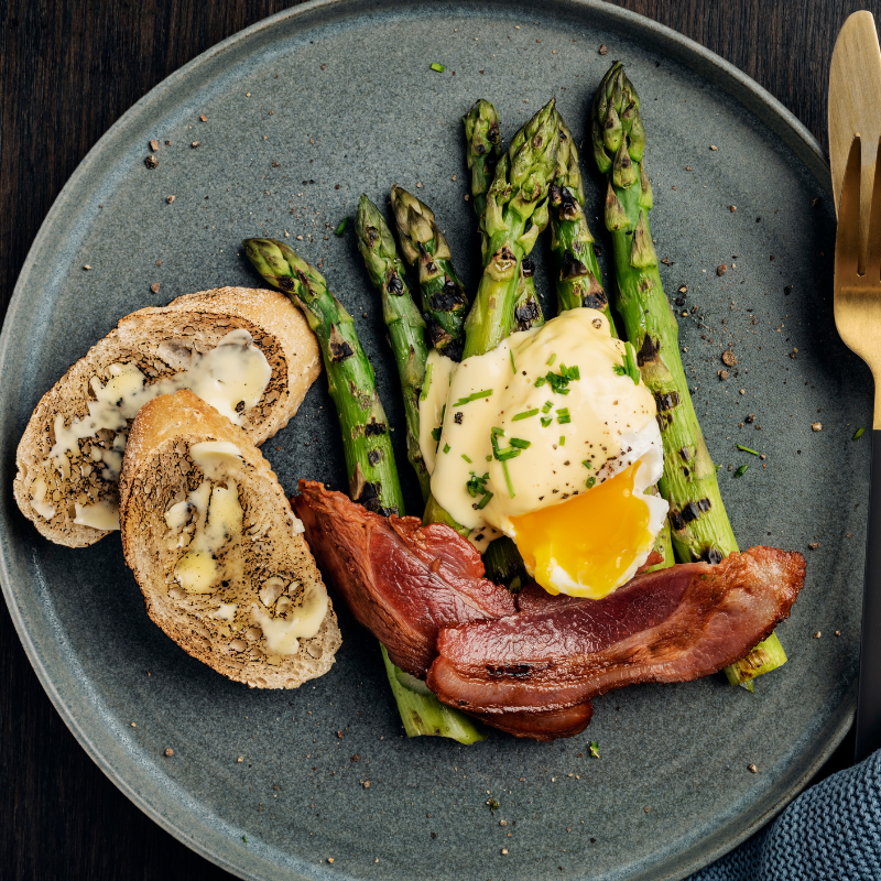 Image showcasing grilled asparagus and bacon served with oysters.
