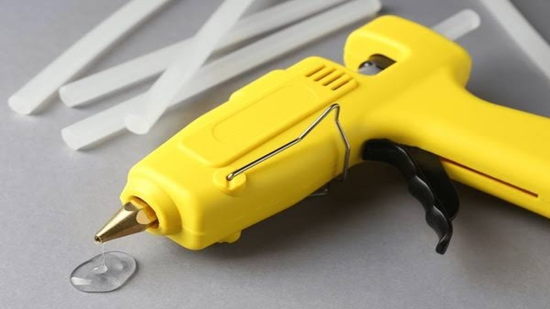 Close-up of a yellow hot glue gun with melted adhesive and glue sticks on a gray background.