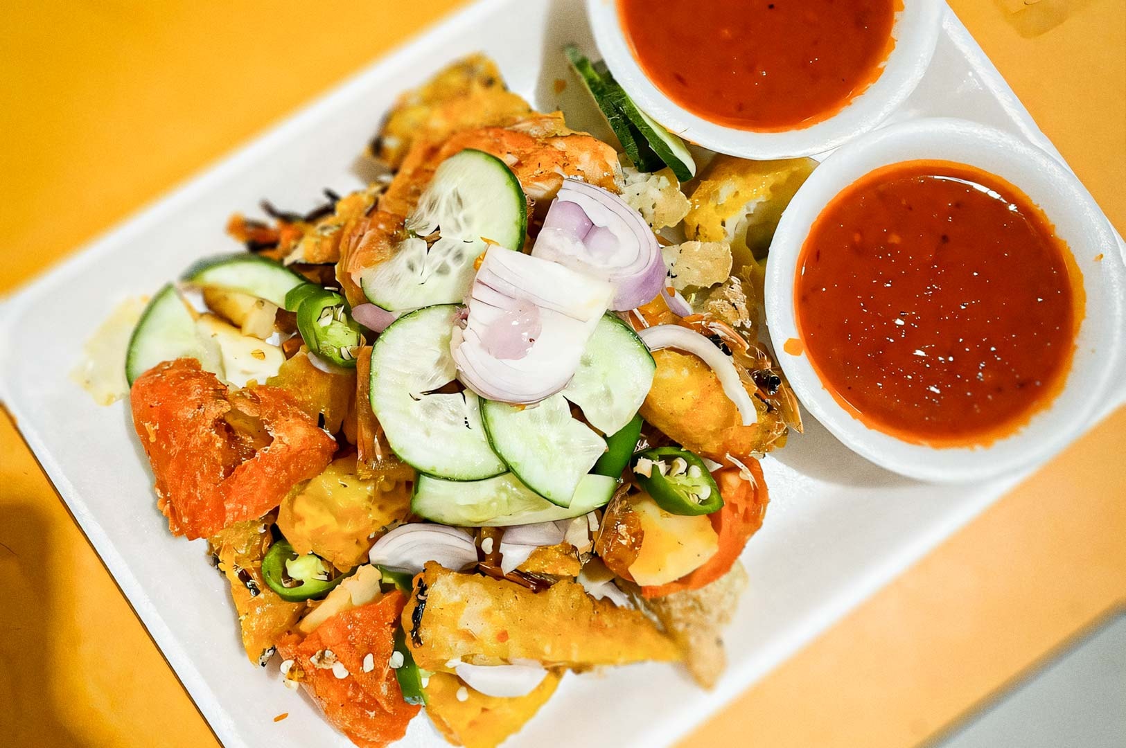 A plate of Indian rojak topped with cucumbers, onions, and green chilies, served with two bowls of bright red dipping sauce.