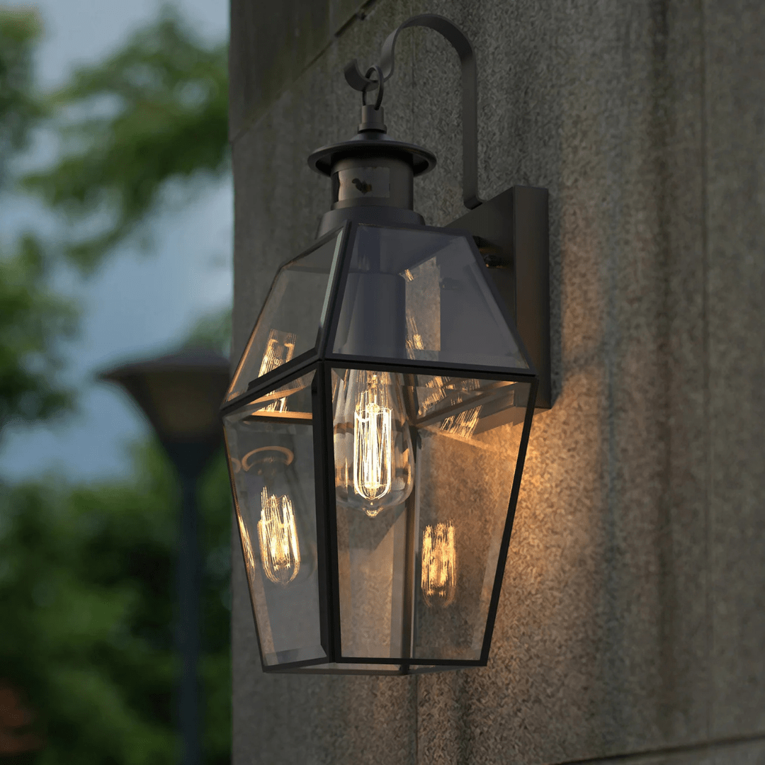 A modern outdoor wall lantern with a black metal frame and clear glass panels, mounted on a stone wall.