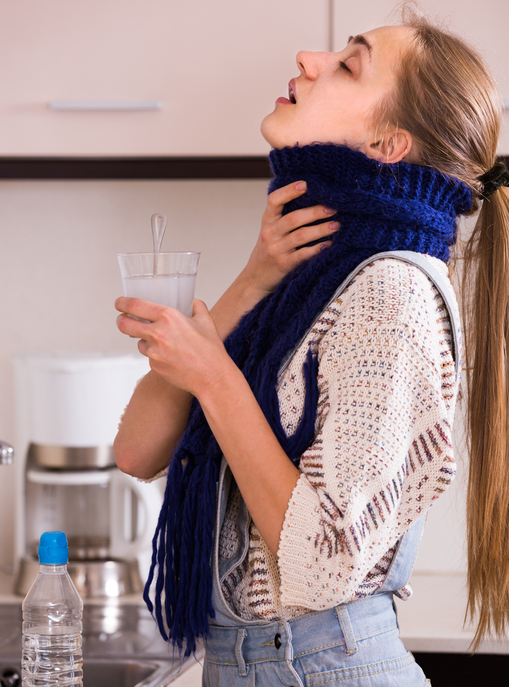 An image of a woman gargling with saltwater in the kitchen. 