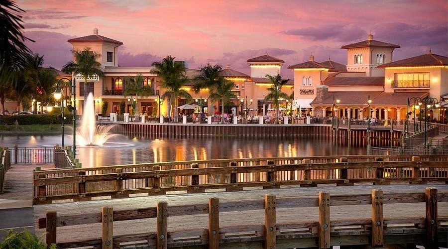 The image depicts a community clubhouse featuring spacious social gathering areas with large windows that offer sparkling lake views, embodying the ultimate Florida lifestyle at Coconut Shores. The inviting atmosphere is enhanced by the surrounding greenery, perfect for peaceful mornings and community events.