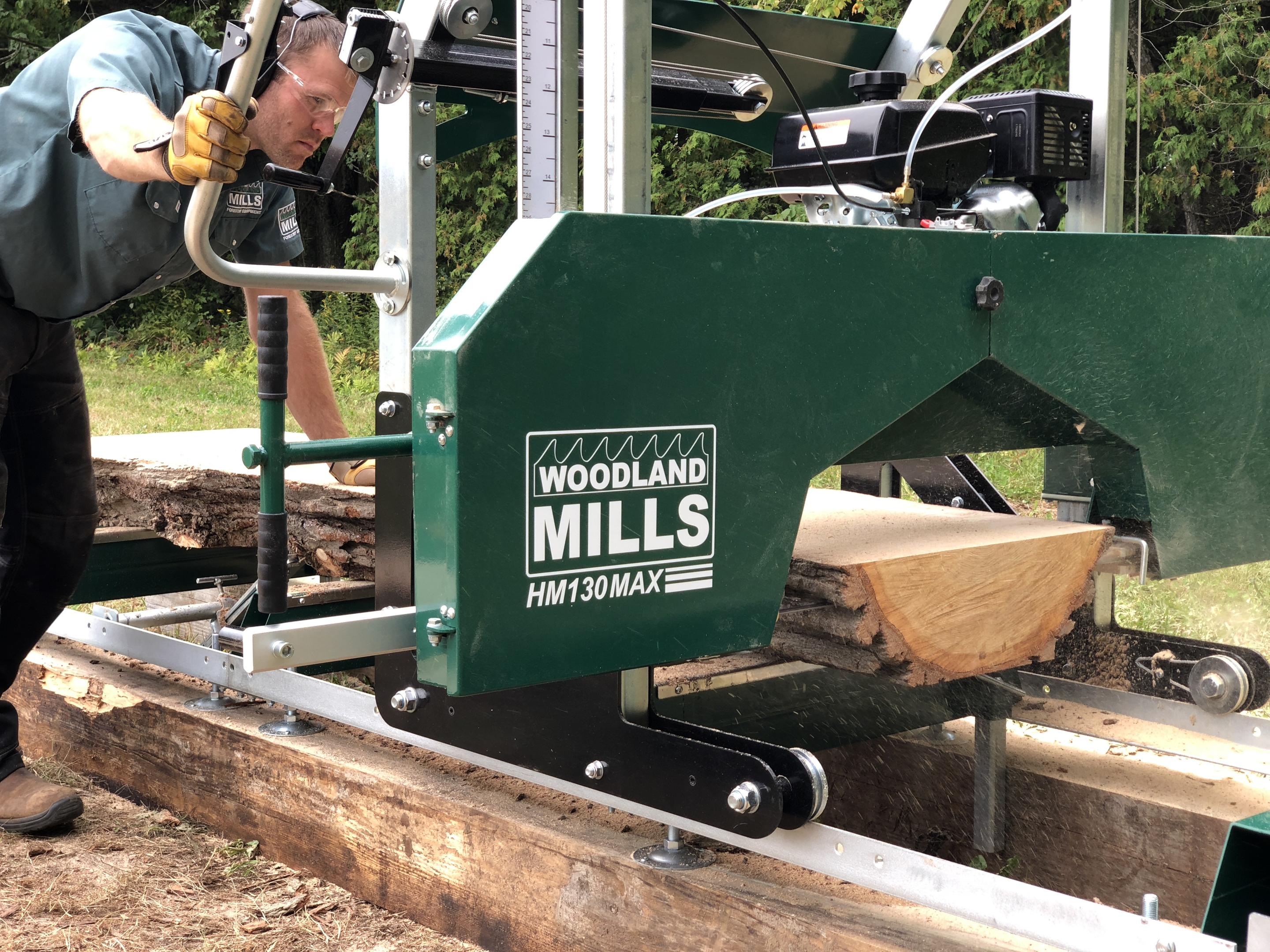 A landowner pushing a Woodland Mills HM130MAX Portable Sawmill through a log to produce a slab.