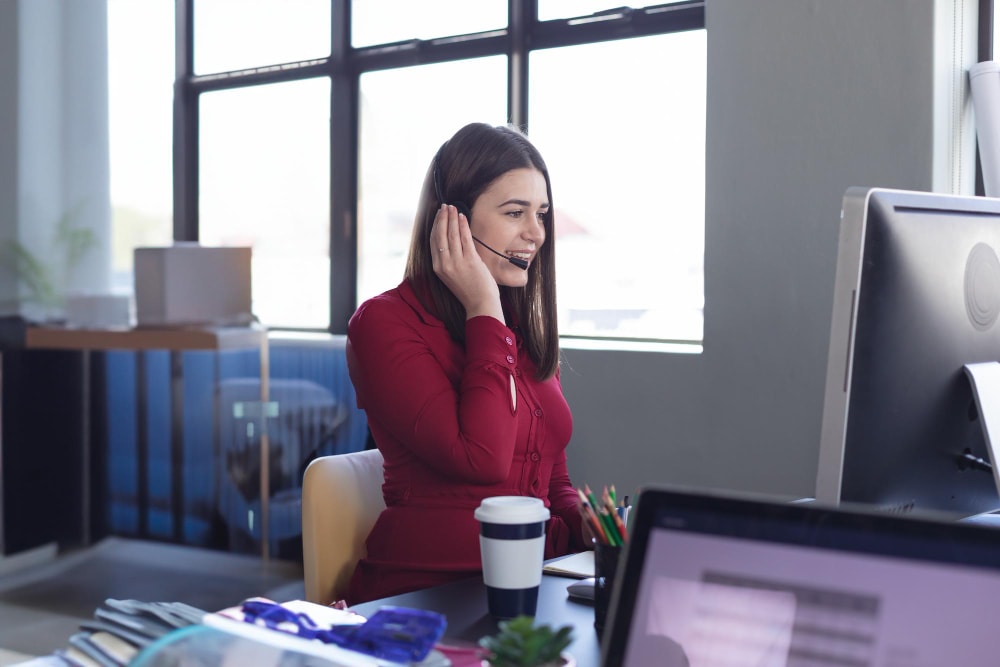 Businesswoman in red dress using headset on incoming calls with a physical phone system.