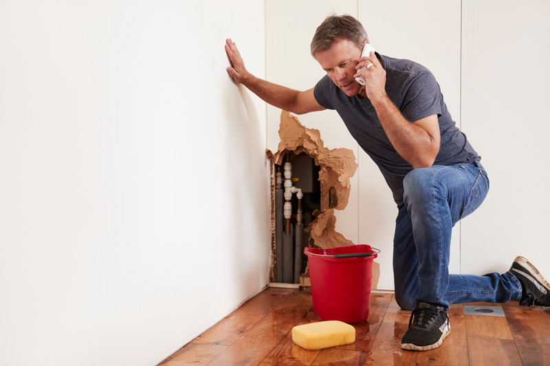 Verzweifelter Mann ruft Installateur Notdienst wegen eines Wasserschadens an der Wand, Eimer und Schwamm vor Ort