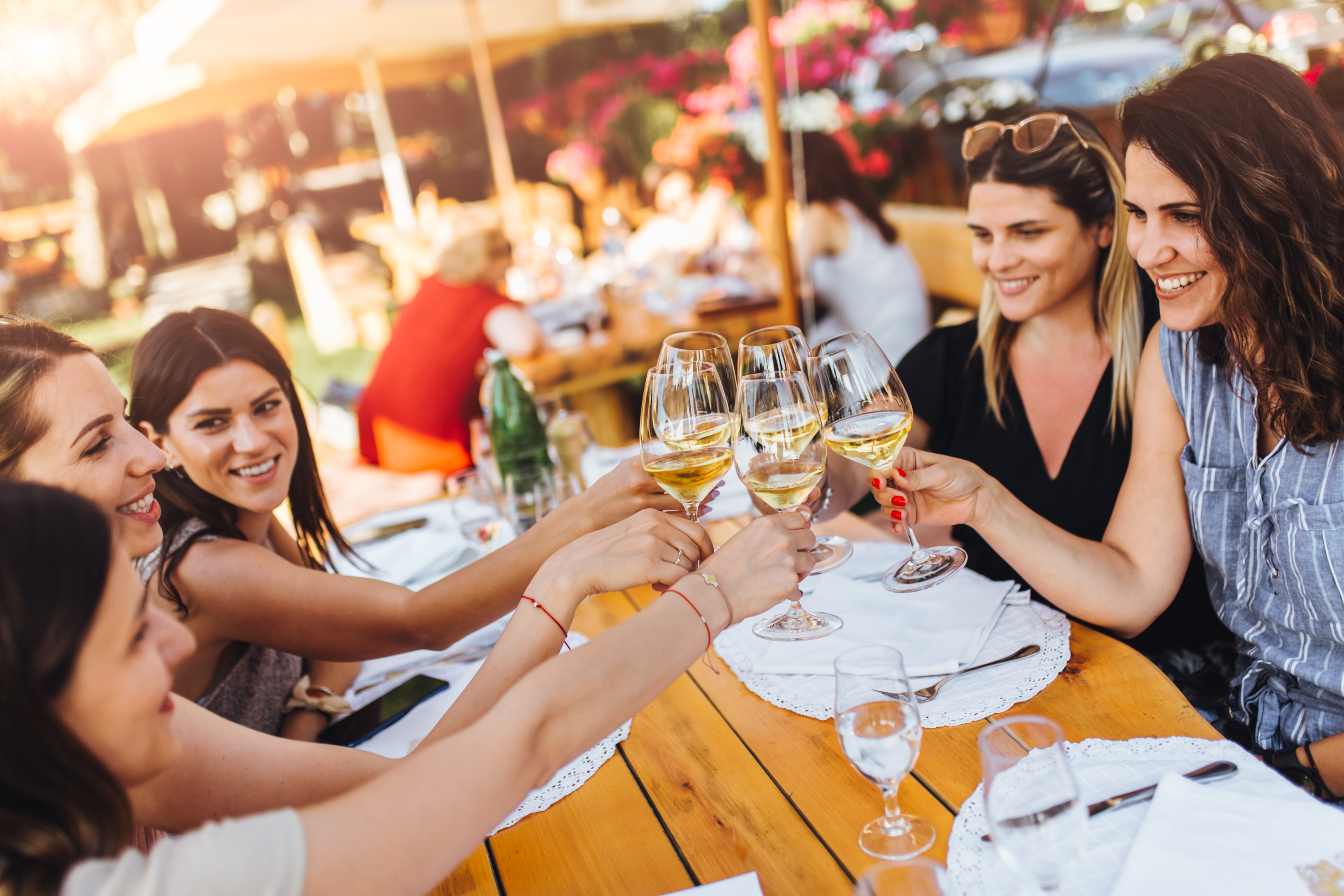 Five women toast with white wine on a patio at a restaurant.