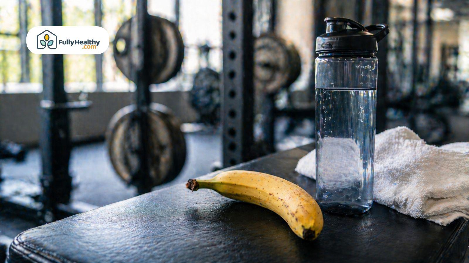 Banana placed next to a water bottle and towel on a gym bench with weights in the background.