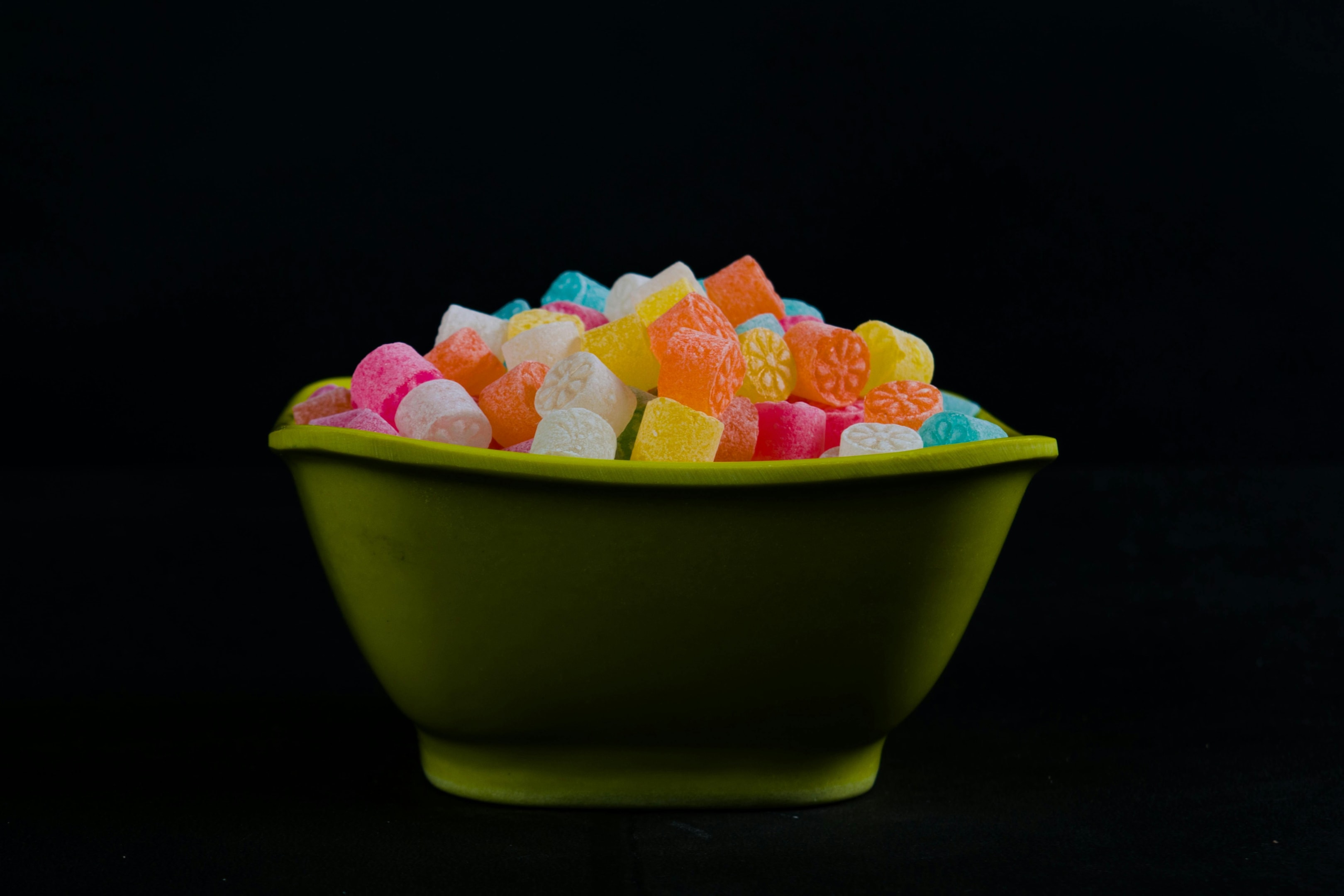 Green bowl filled with colorful, fruit-patterned gummy candies against a black background, showcasing vibrant textures and variety.