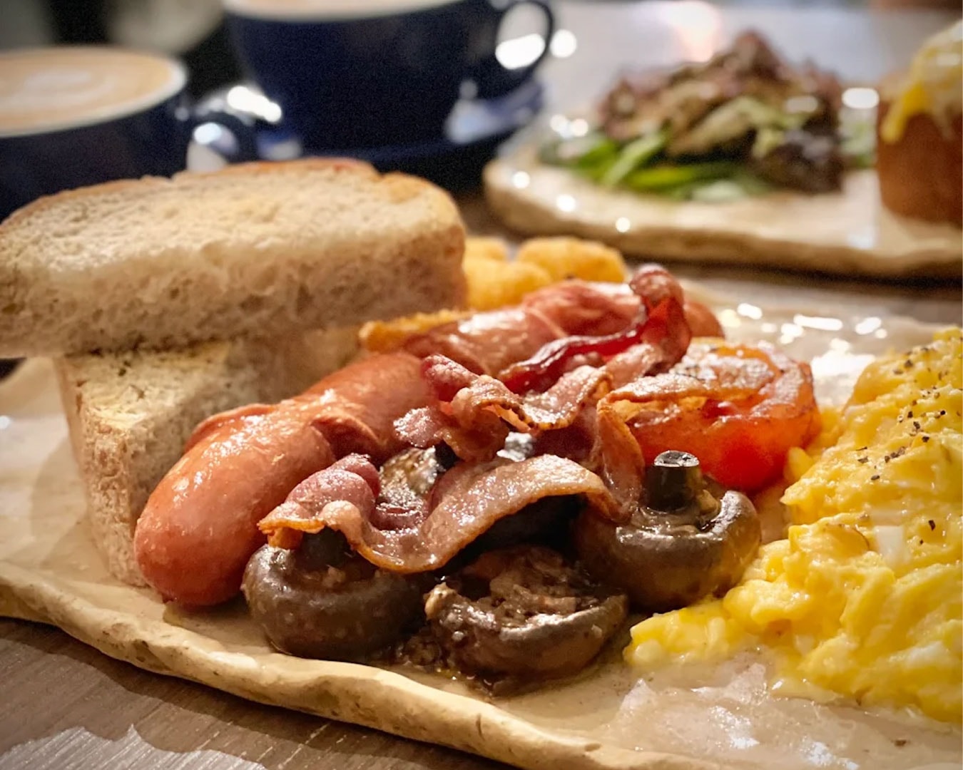 A generous breakfast spread featuring crispy waffles paired with streaky bacon and a classic platter of eggs and sides, ideal for a hearty morning meal.