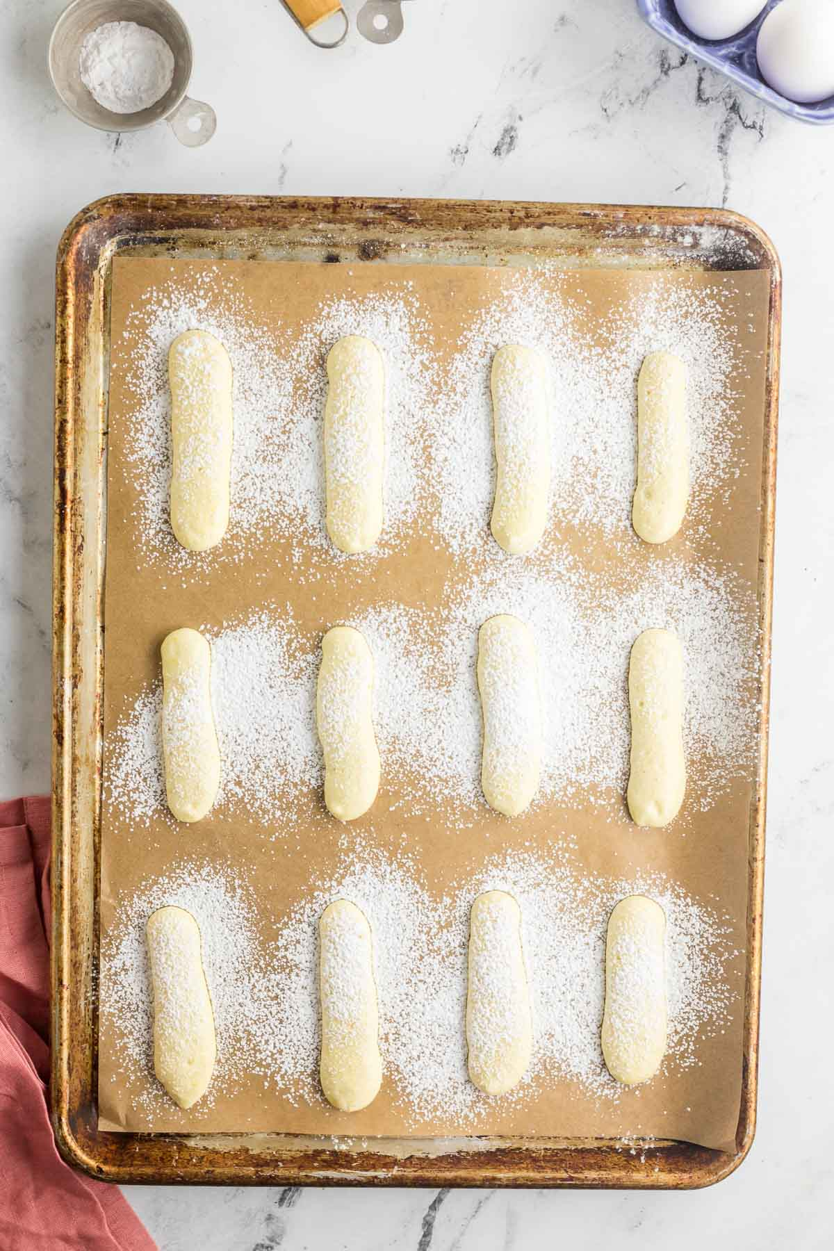 baking sheet of piped lady finger cookies dusted with powdered sugar