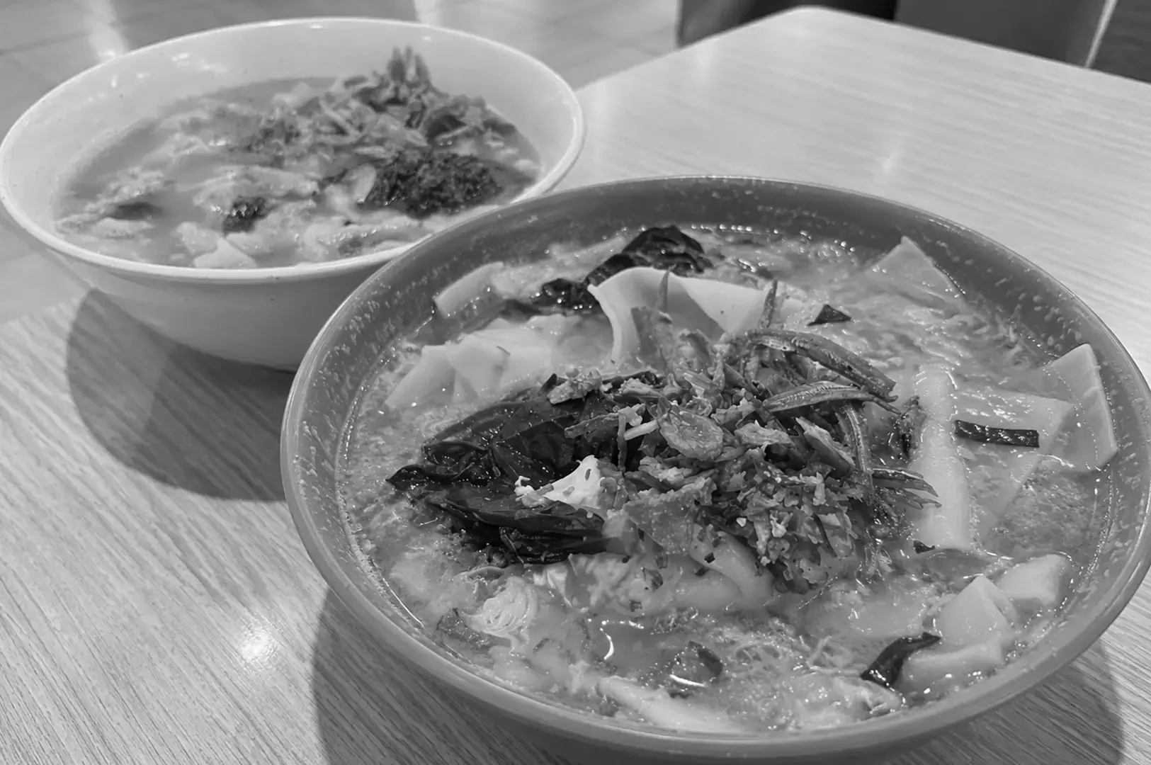 A bowl of handmade wheat noodles served with minced meat, leafy greens, and assorted toppings in a comforting soup.