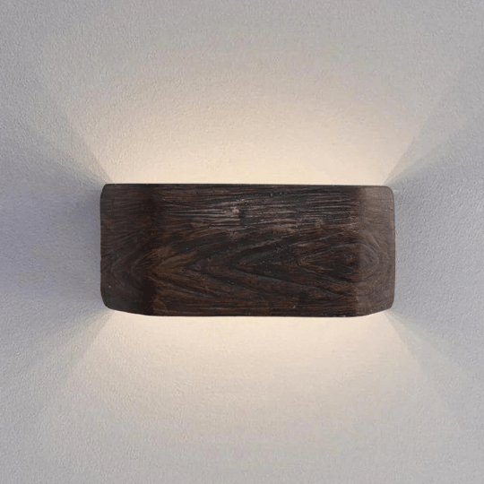 Modern farmhouse wall sconce with a dark wood finish, mounted on a light-colored wall, emitting soft light both upward and downward for a warm, inviting glow.