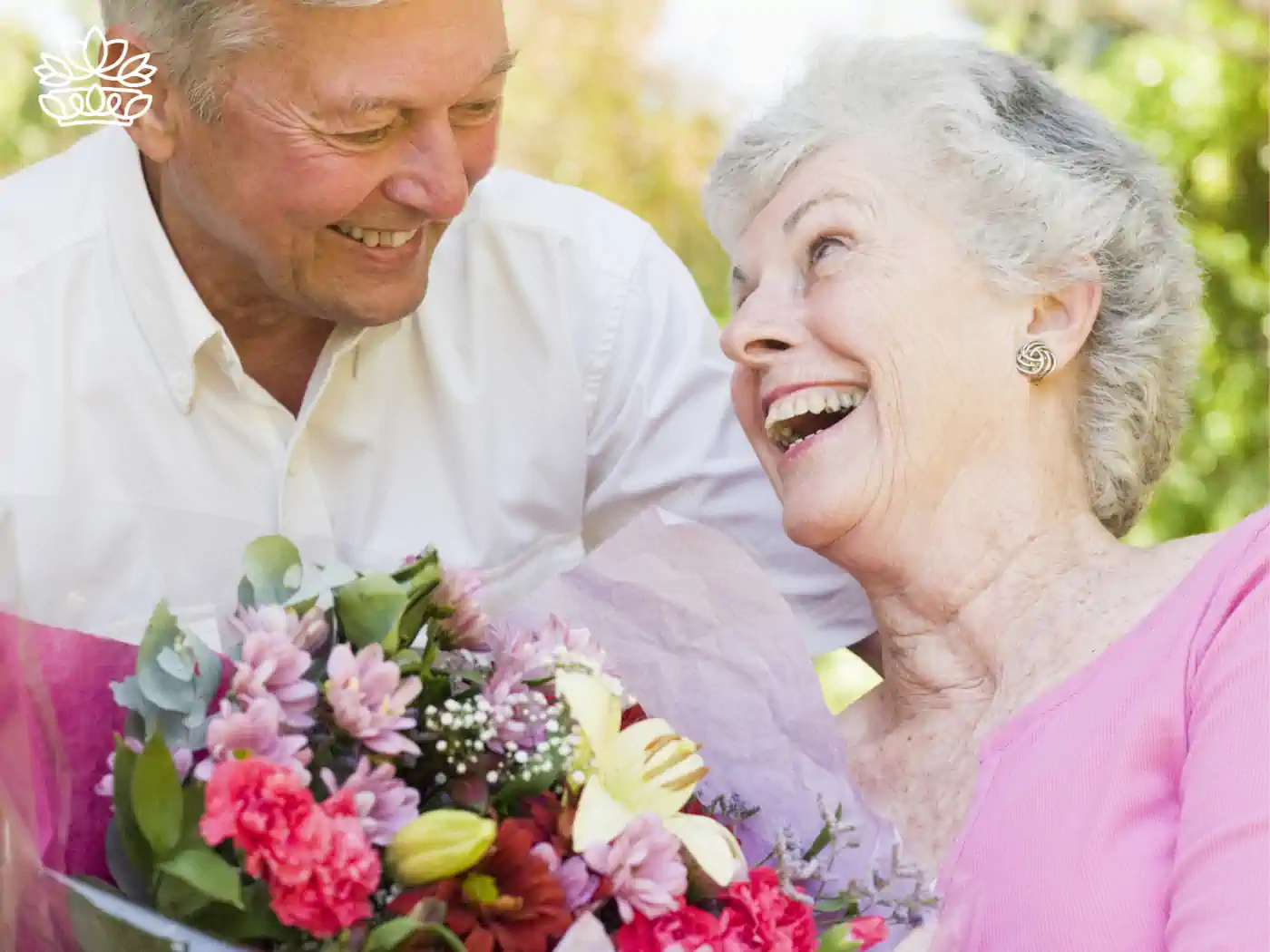 Elderly man joyfully presenting a colourful bouquet of flowers to an elderly woman, both sharing a laugh in a sunny garden. Just Because Flowers. Delivered with Heart. Fabulous Flowers and Gifts