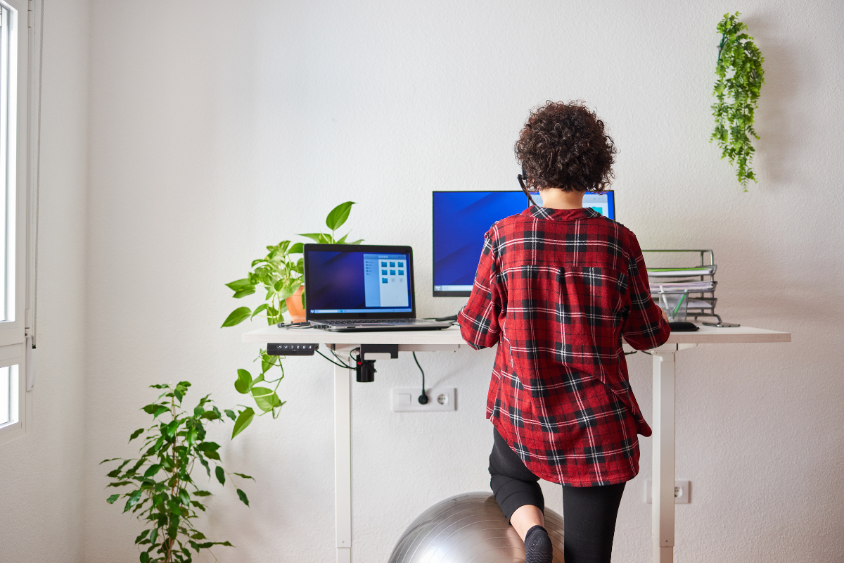 Women standing at her stand up desk with a exercise ball.
