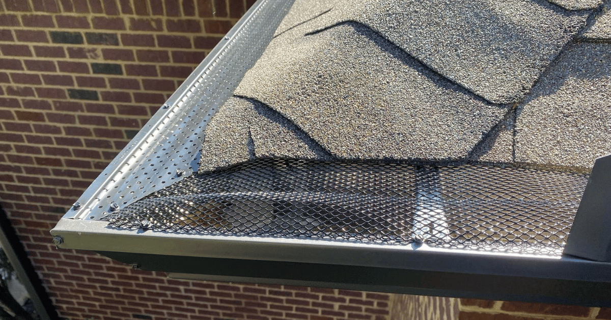 Close-up of a roof's edge showing shingles and a mesh gutter guard system protecting from debris.