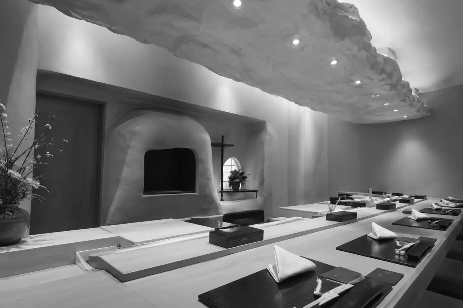 Elegant Japanese sushi counter featuring a sculpted textured ceiling, minimalist seating, wood surfaces, and an open preparation area.