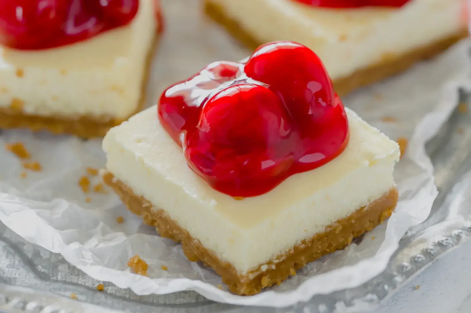 A close-up of cheesecake squares topped with cherry glaze, placed on a silver platter.