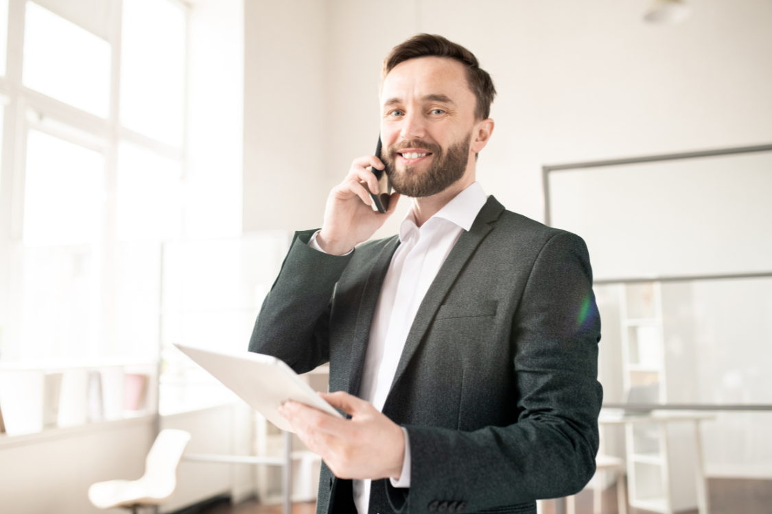 Confident business broker making a call while holding a tablet to connect with qualified buyers