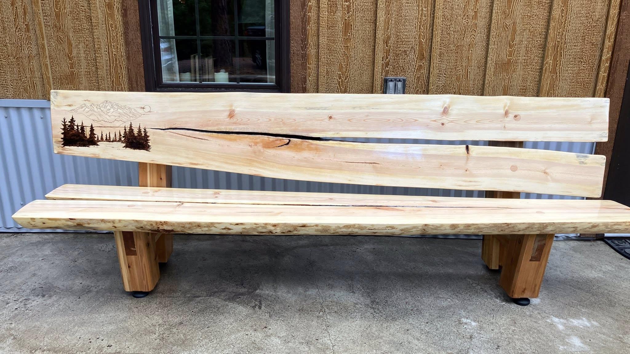 A bench with a split log and a design of trees burned into it. 