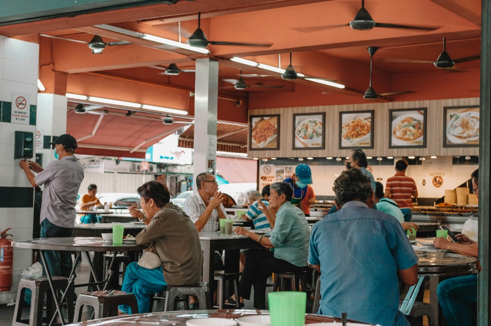 A lively scene of people dining at a Singapore Hawker Centre, with a busy market atmosphere in the background.