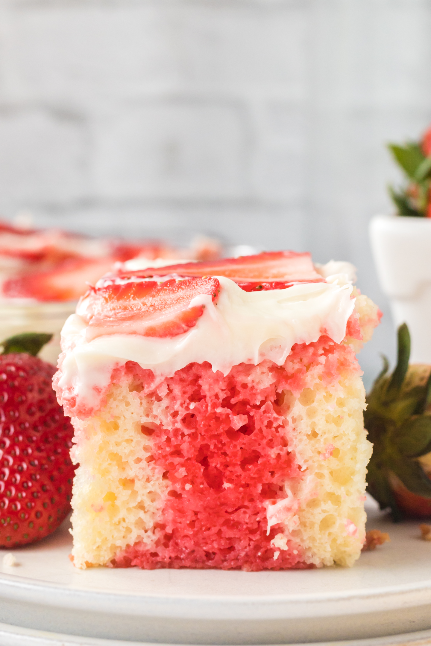 slice of strawberry poke cake on a plate topped with fresh strawberries slices