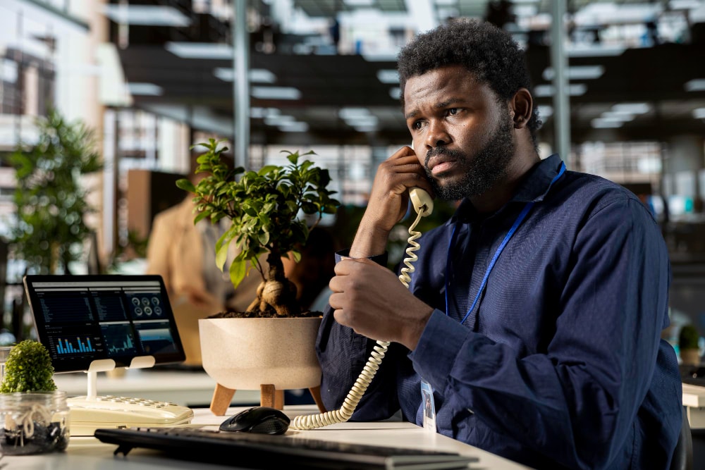 A customer service worker answering a landline phone call at his workstation but seriously needing a robust unified communications solutions.