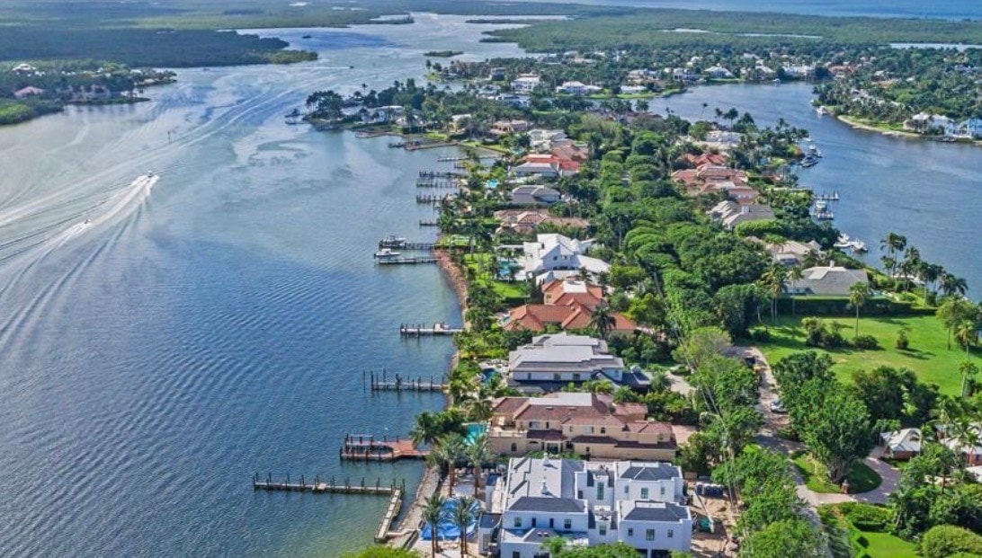 A luxury yacht is docked at a stunning waterfront estate in the prestigious Port Royal neighborhood, providing direct access to the Gulf of Mexico through the canal system. The residence features expansive outdoor living spaces and serene waterfront views, epitomizing luxurious waterfront living in Naples, FL.