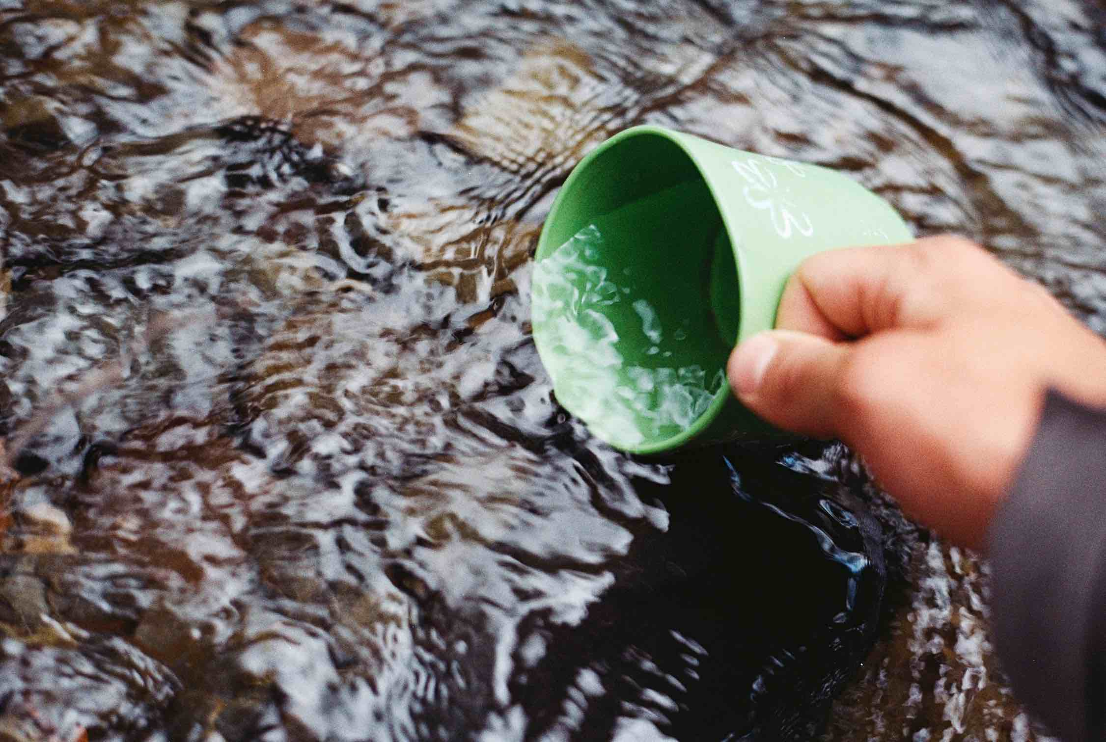 Person, die Wasser aus einem Bach schöpft