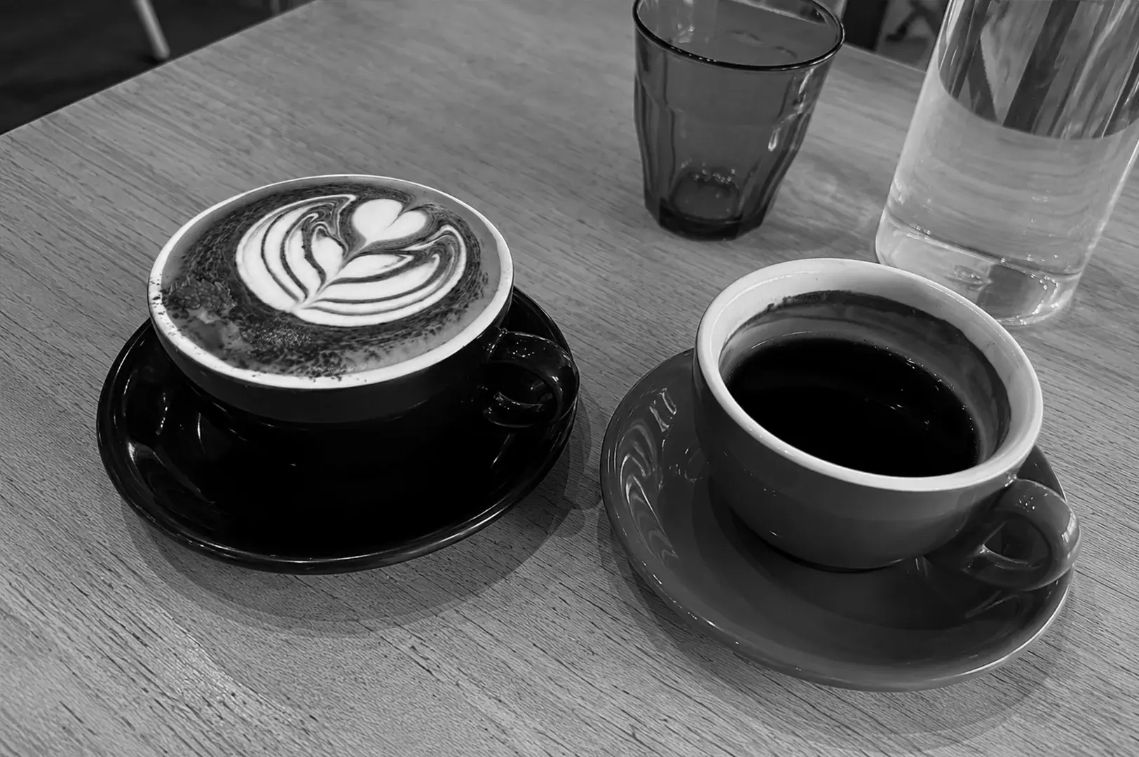 Cappuccino with latte art and a cup of black coffee served together on a wooden café table.