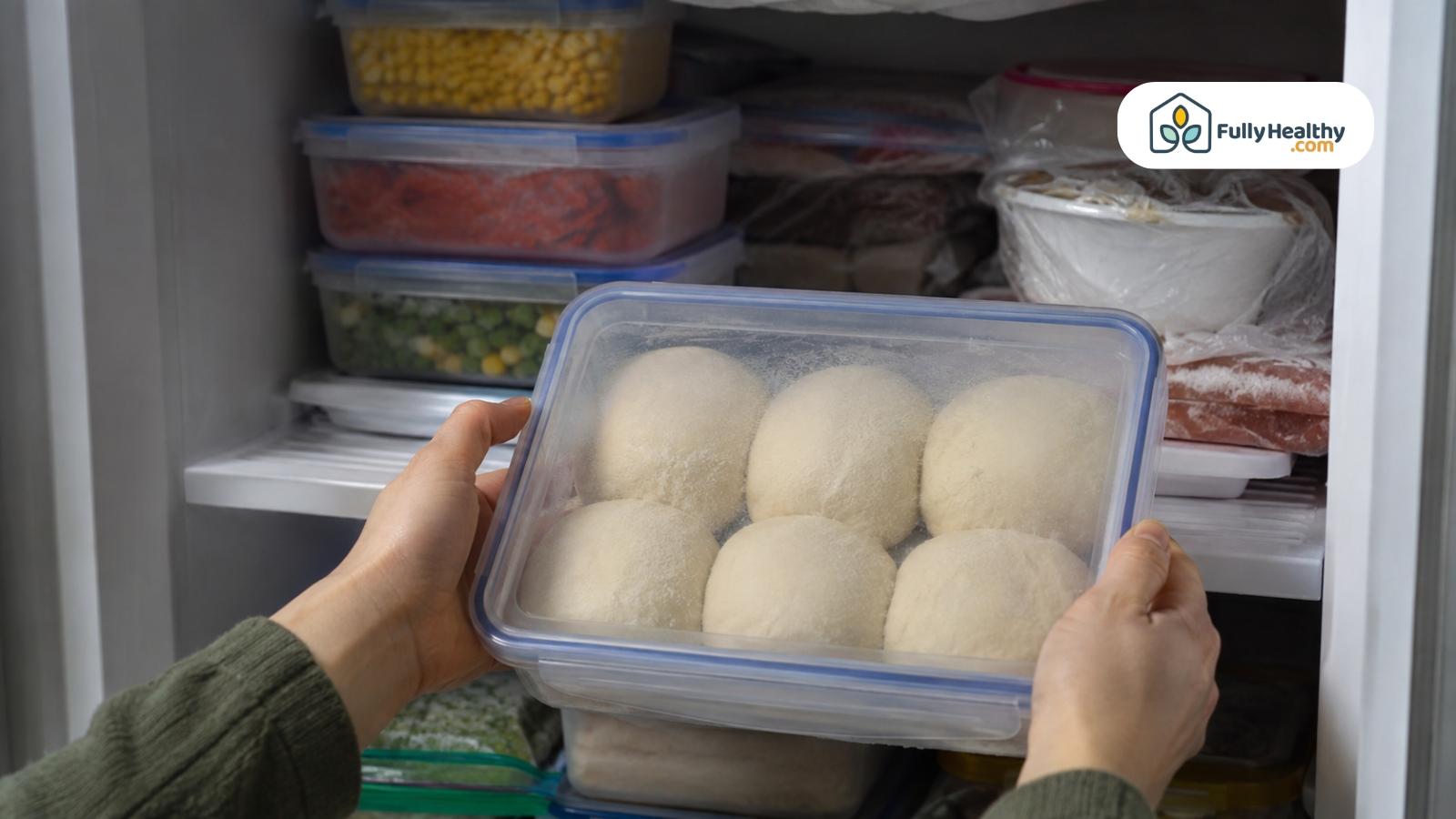 Container of pizza dough balls being placed inside an organized freezer