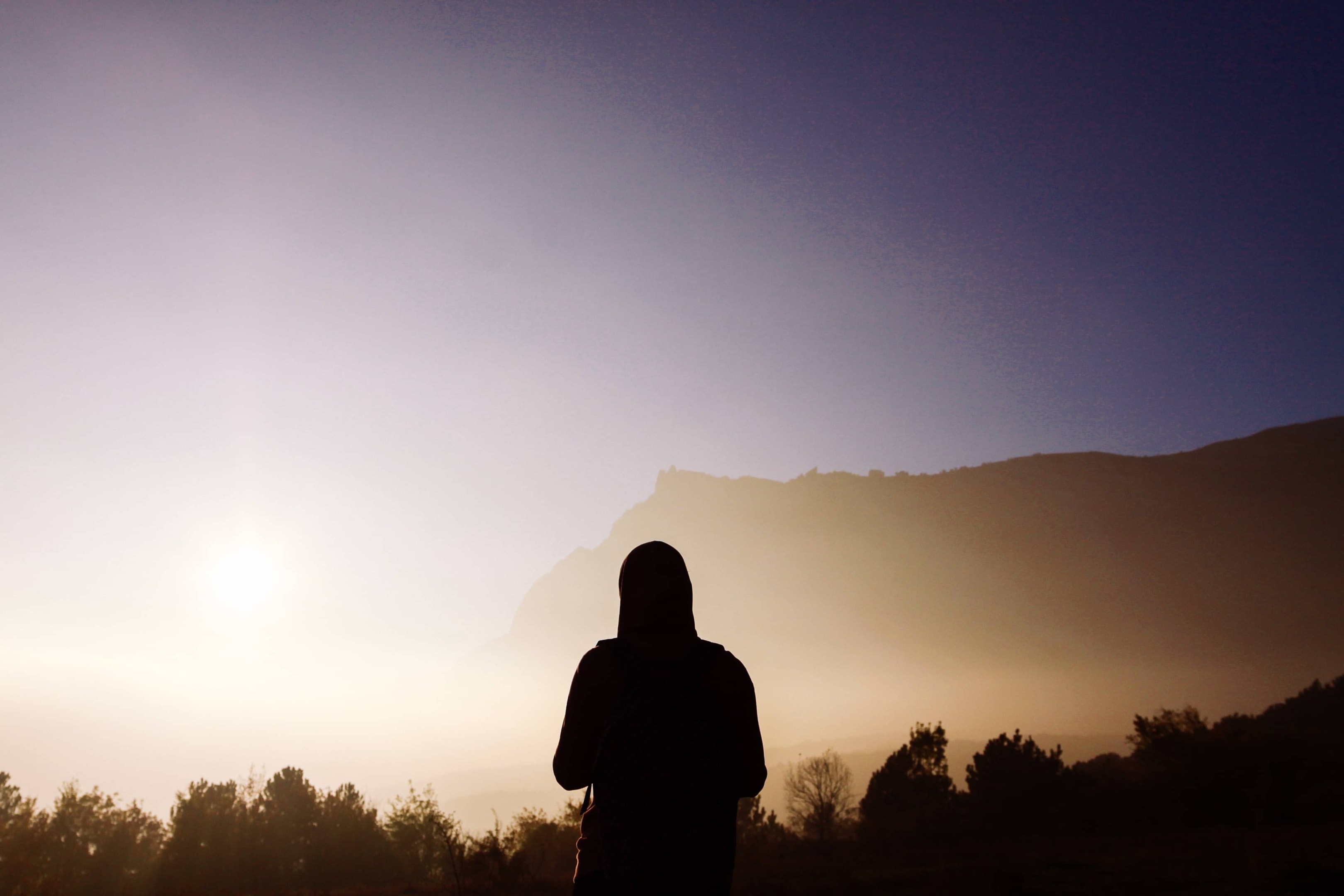 A person standing alone at sunrise near a mountain, reflecting on life and finances, symbolizing the freedom that comes from wisely managing flexible expenses.
