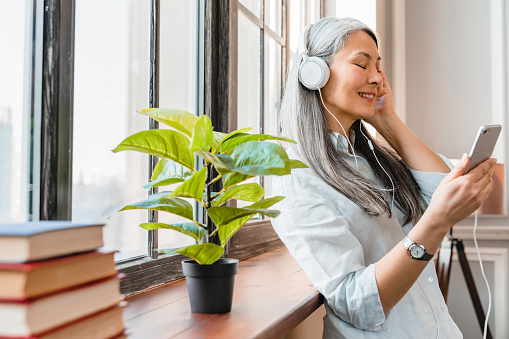 Woman with long gray hair wearing headphones and listening to a podcast.