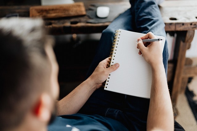 A man writing in a notebook in preparation for a creative writing competition.
