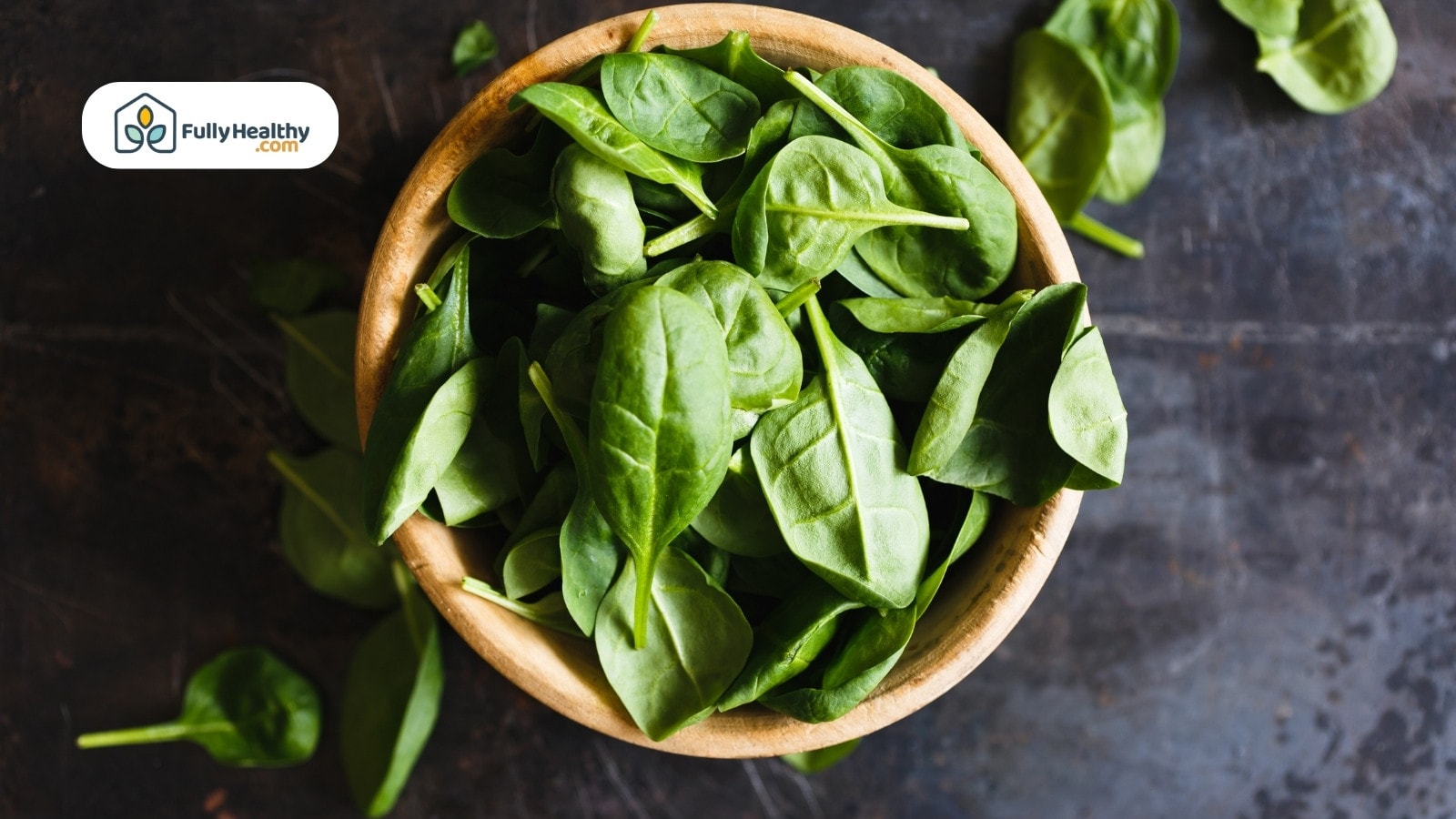 Fresh spinach leaves in wooden bowl on dark rustic background