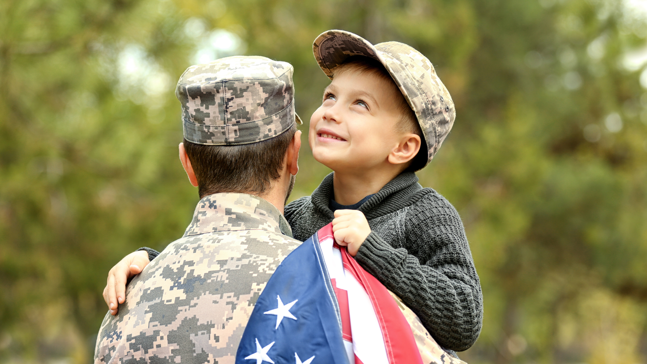 Military dad holding his young son in his arms with an American flag in hand.