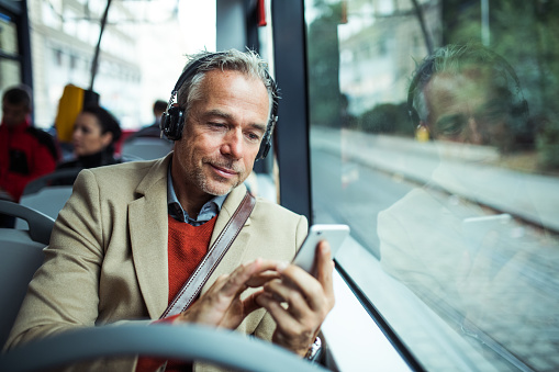 Mature man on a bus listening to a podcast on his cell phone. 