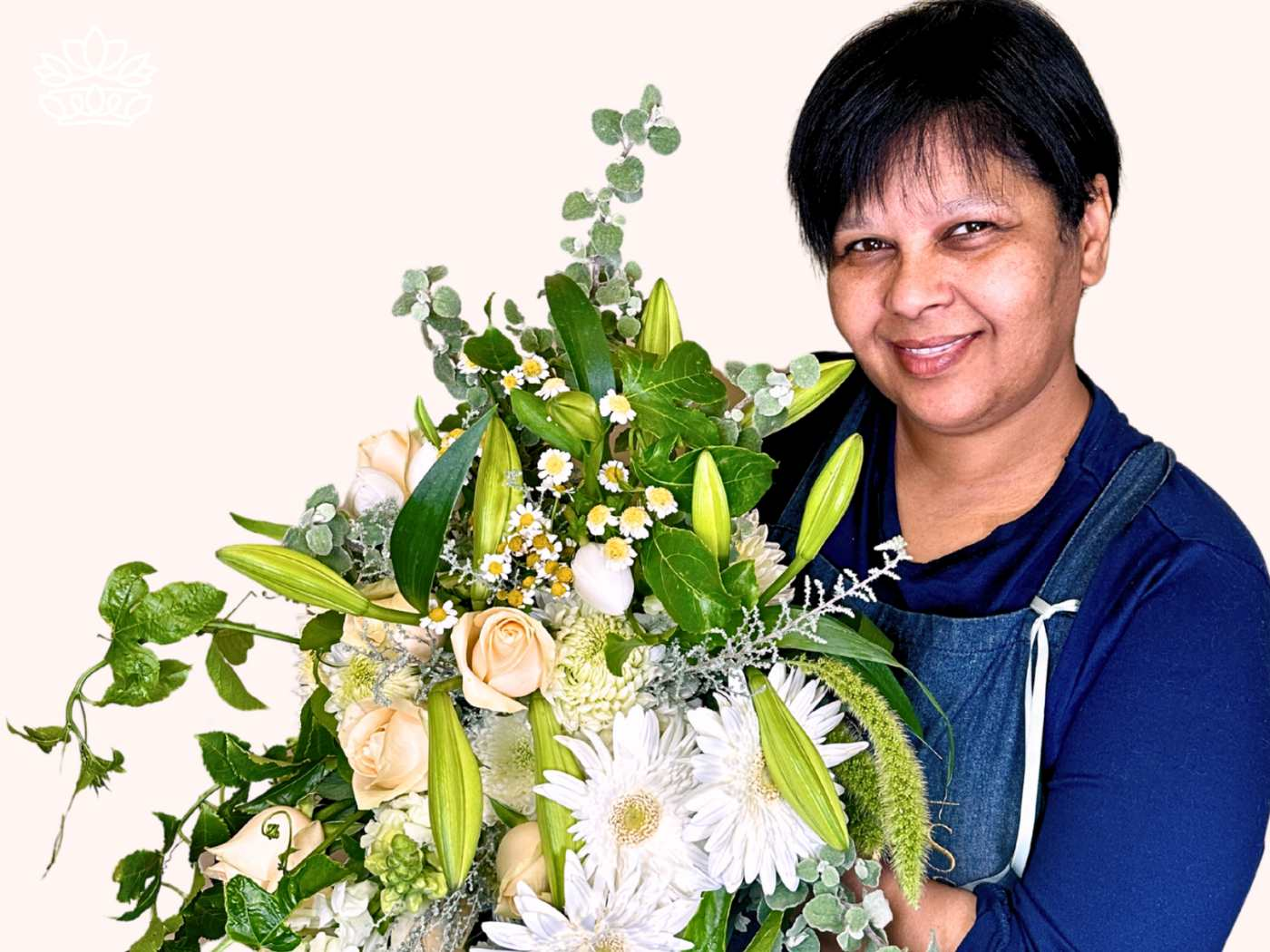 Cheerful florist holding a quality bunch of blooms from the Florist Choice Bouquets Collection, featuring cream roses, white lilies, and lush foliage. Perfect for delivering flowers that delight customers. Fabulous Flowers and Gifts.