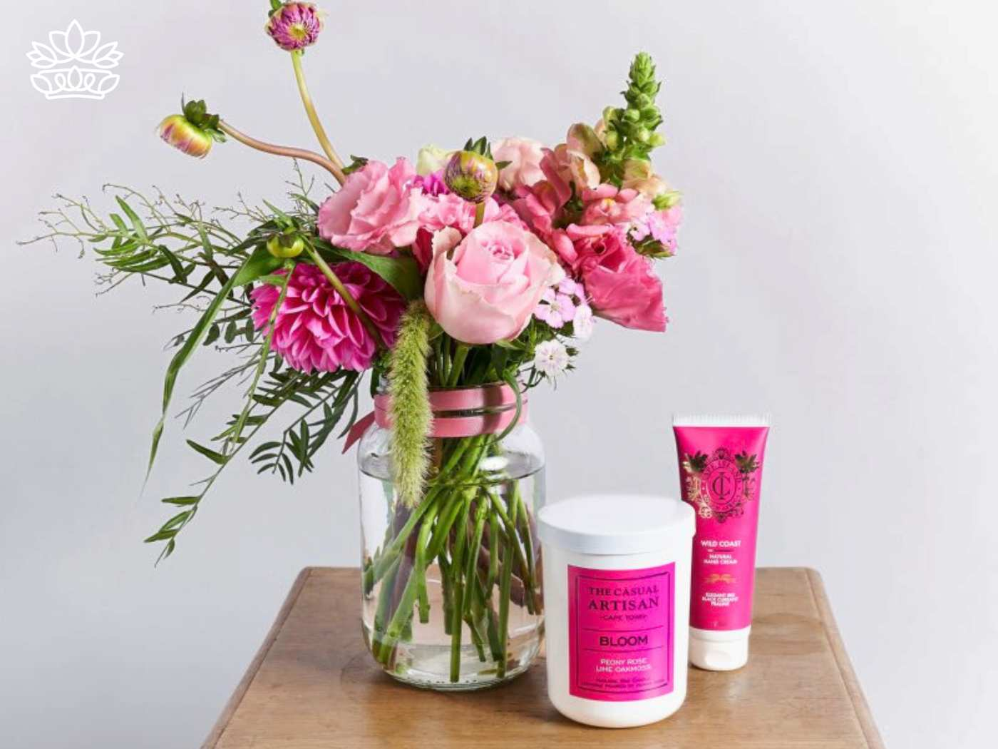 A spa-themed gift set featuring a jar of natural hand cream, a floral-scented candle labeled 'Bloom,' and a bouquet of pink flowers in a mason jar, representing a thoughtful gesture of care and relaxation. Fabulous Flowers and Gifts. Gifts for Her.