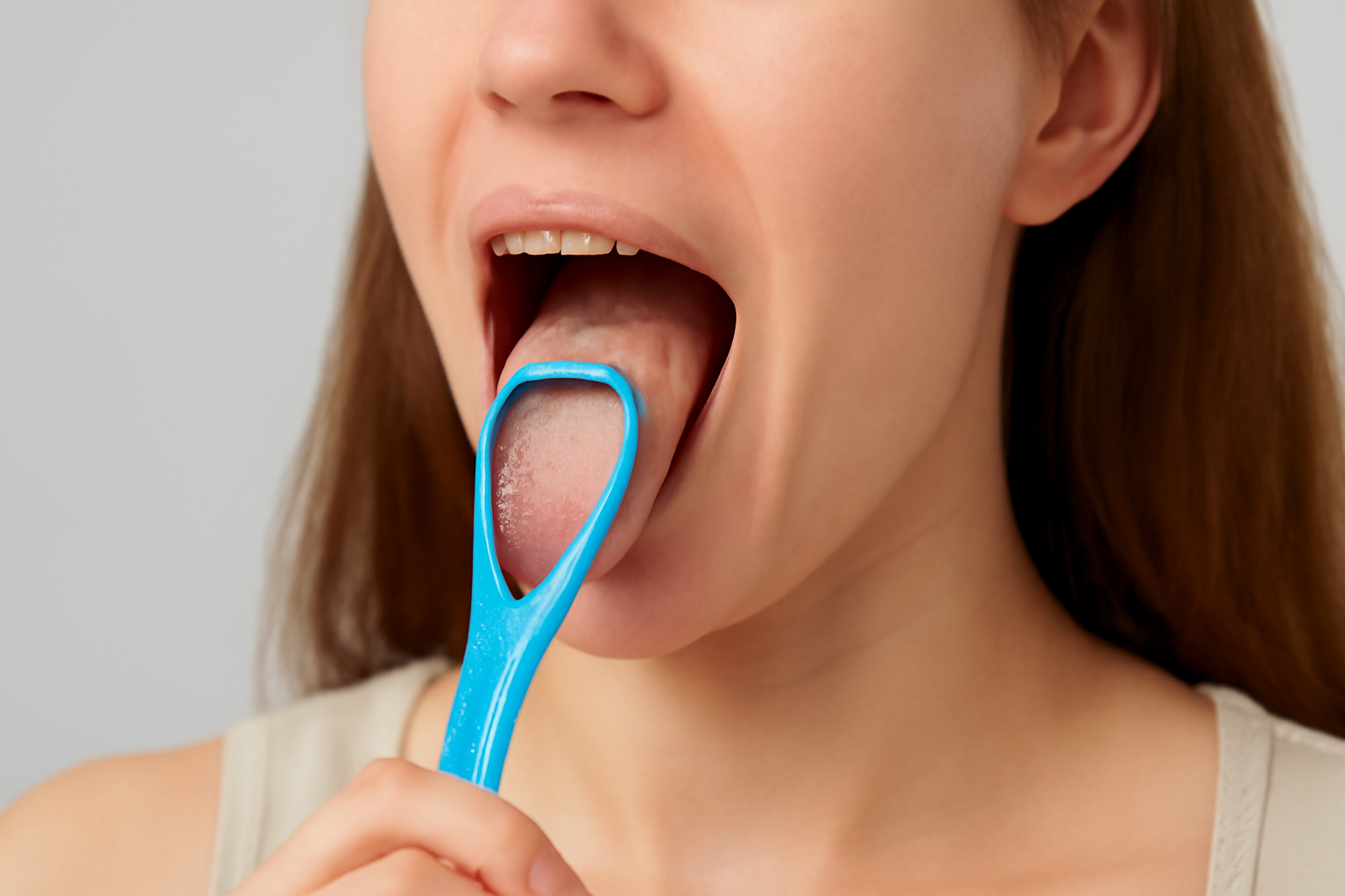 En ung kvinne utfører munnhygiene med en blå tungeskrape, og fjerner belegget fra tungen.
