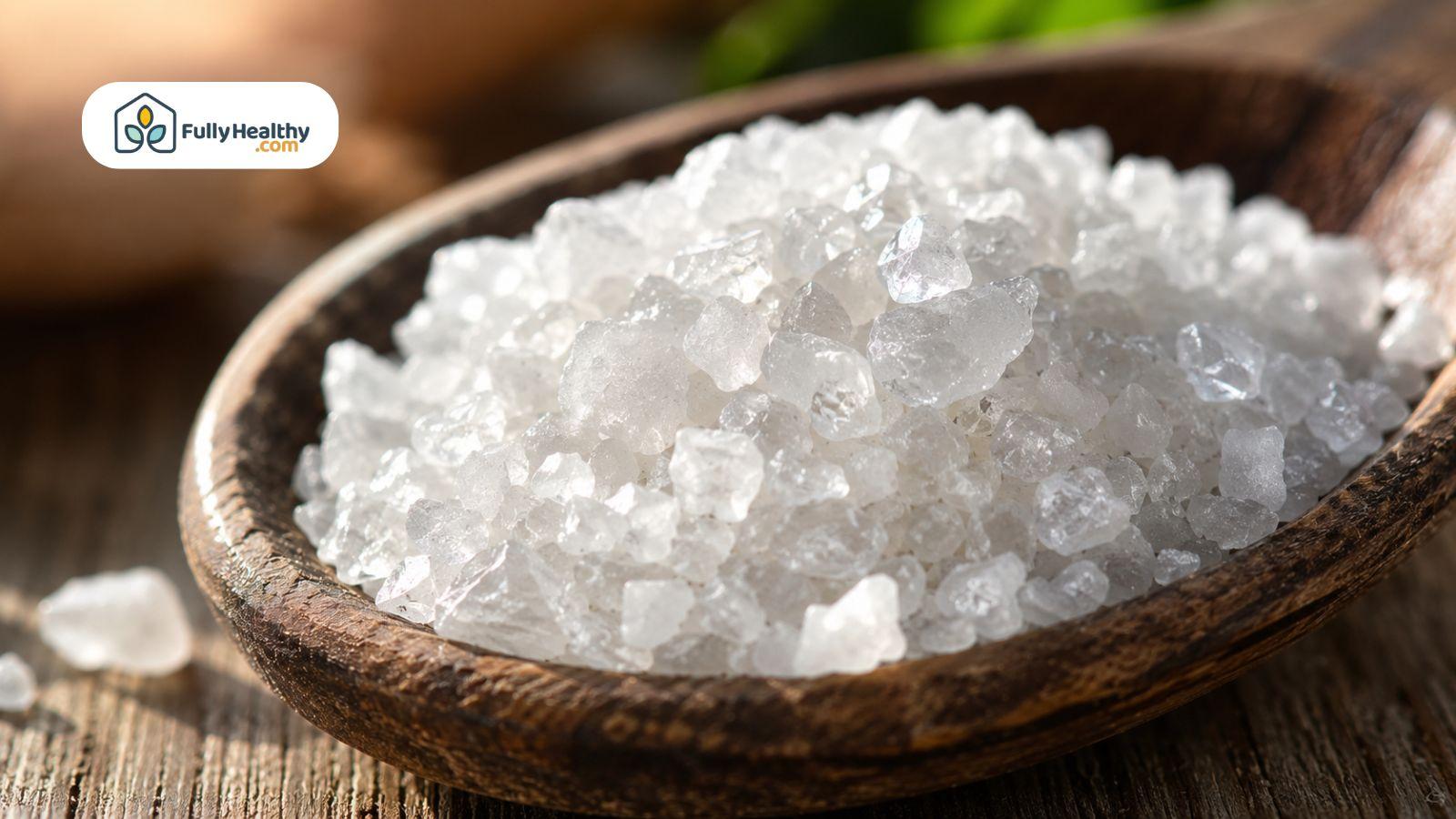 Close-up of coarse sea salt crystals resting on a rustic wooden spoon.