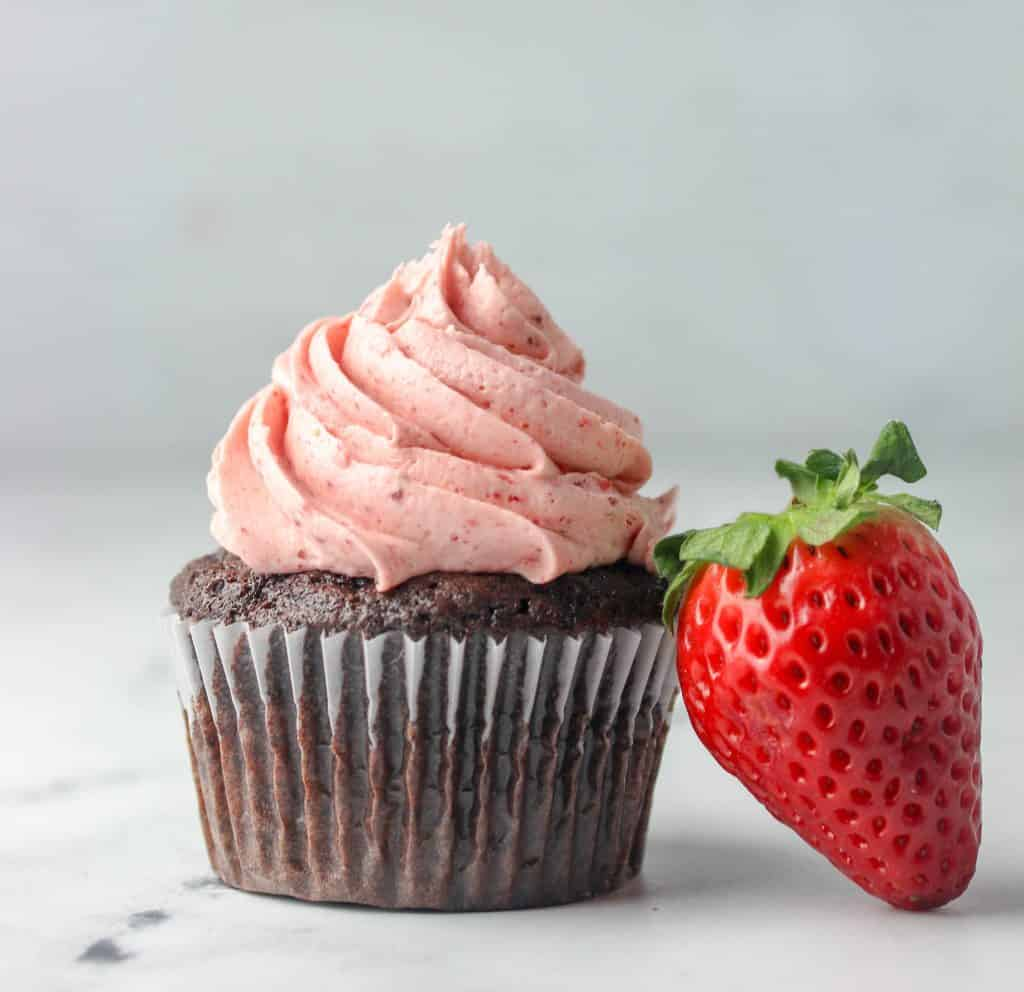 chocolate cupcake with strawberry buttercream frosting with a strawberry next to it