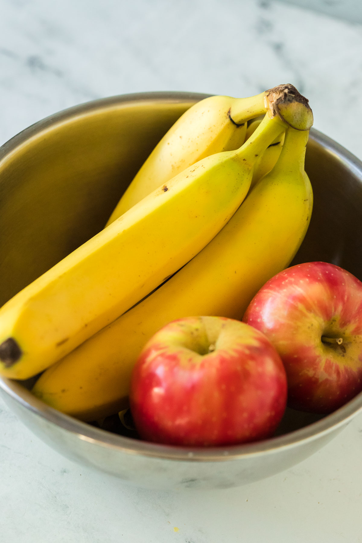 a bunch of bananas in a bowl with two apples