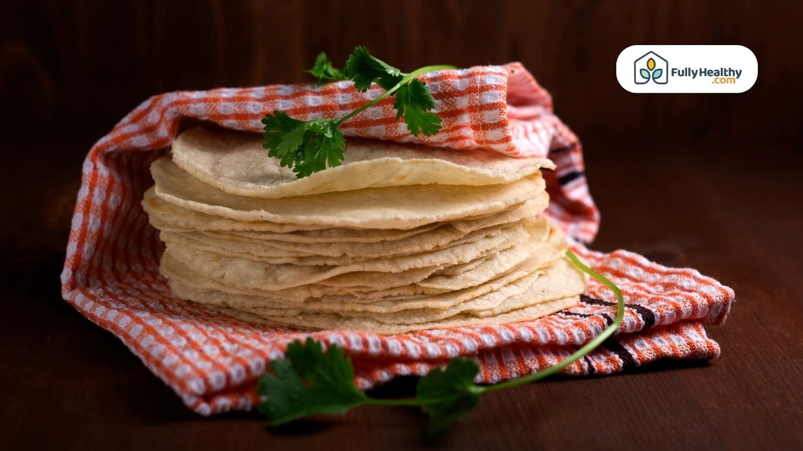 Stack of uncooked tortillas wrapped in a red checkered cloth, garnished with cilantro
