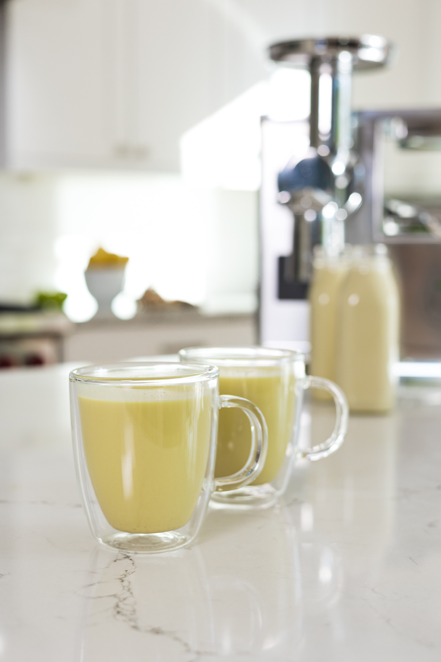 Two glass mugs hold warm golden milk, or turmeric milk, a delicious beverage made from homemade almond milk.