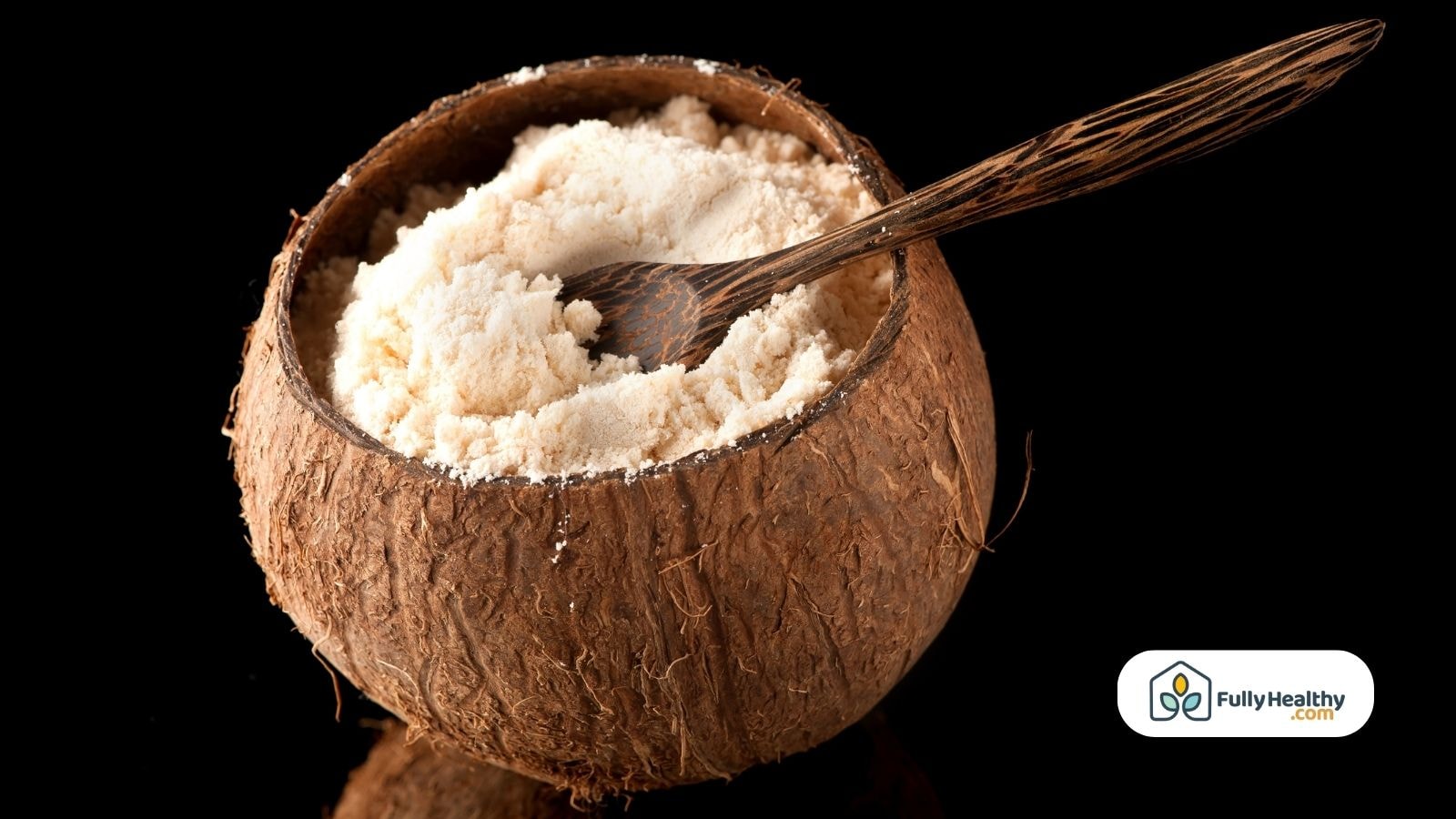 Coconut flour in half coconut shell with wooden spoon on black background