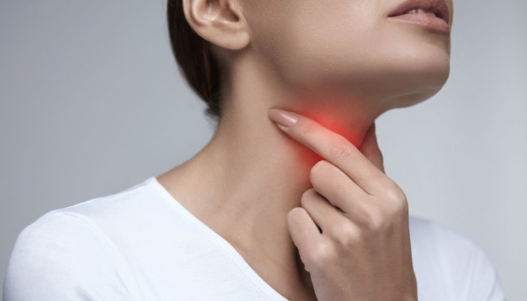Kvinne holder seg på halsen med smerteuttrykk, rød belysning markerer området for sår hals eller betennelse.