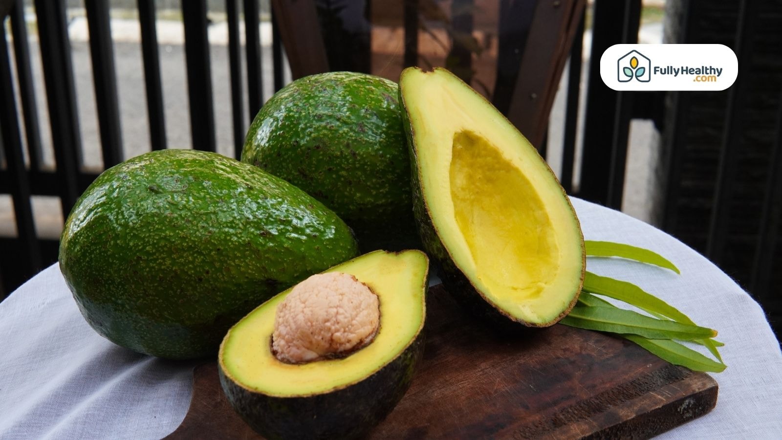 Fresh green avocados with halved fruit on wooden board
