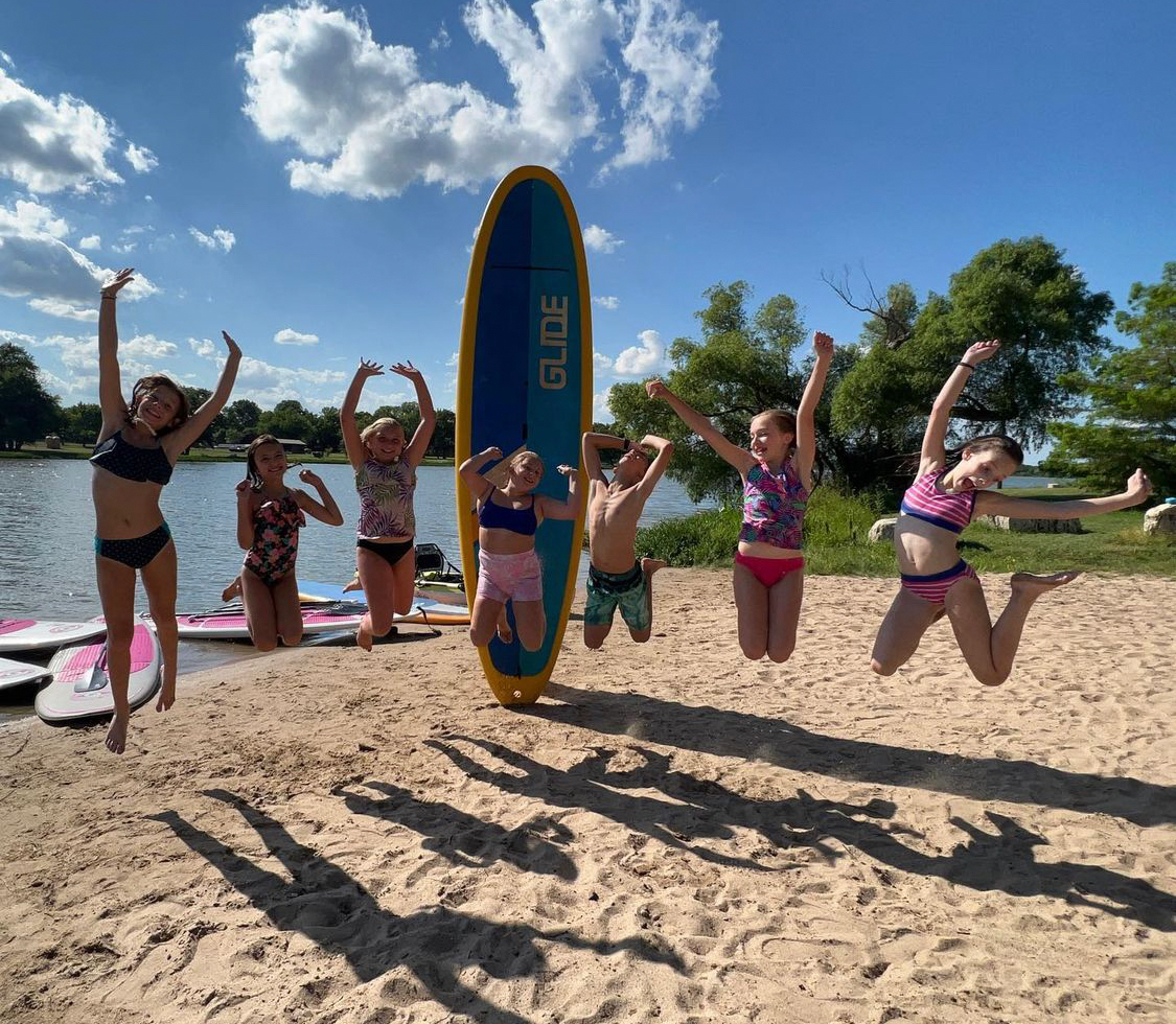 girls jumping around a stand up paddleboard
